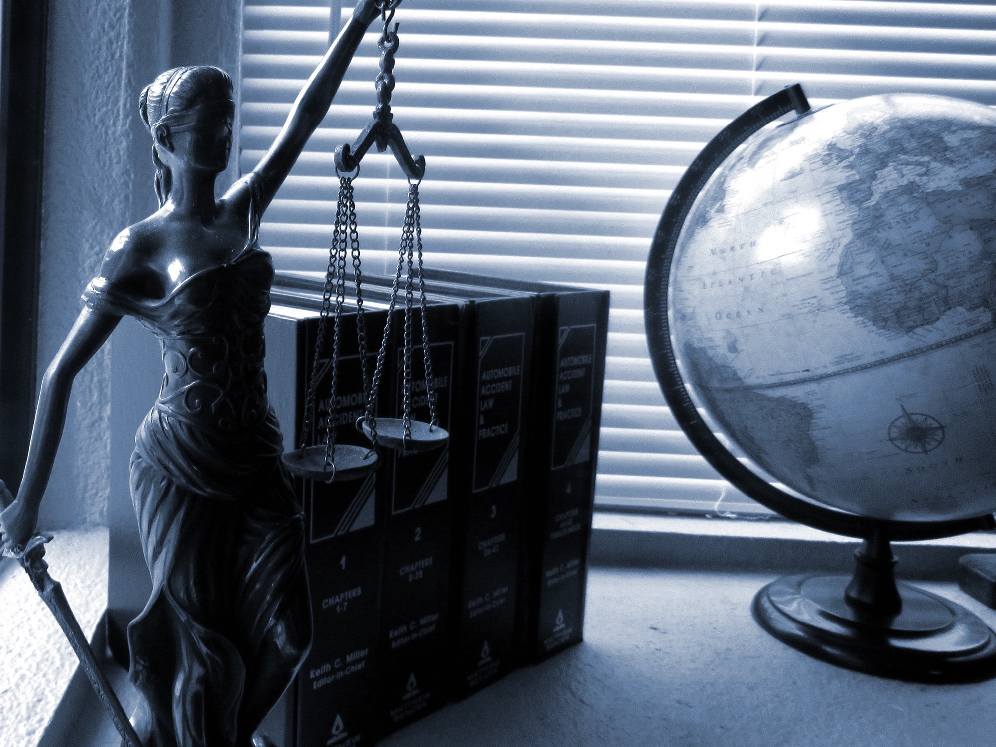 Foto: Justitia-Statue, juristische Bücher und ein Globus auf einem Schreibtisch
