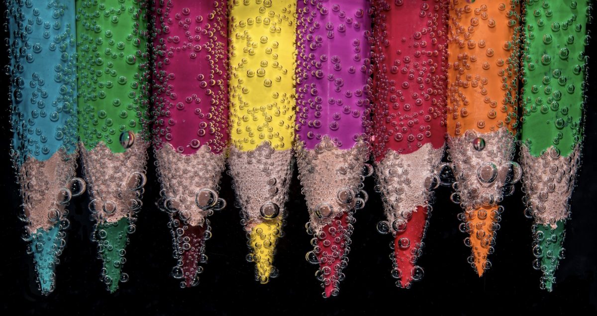 Foto: Reihe von Buntstiften, die unter Wasser liegen und von Luftbläschen umgeben sind