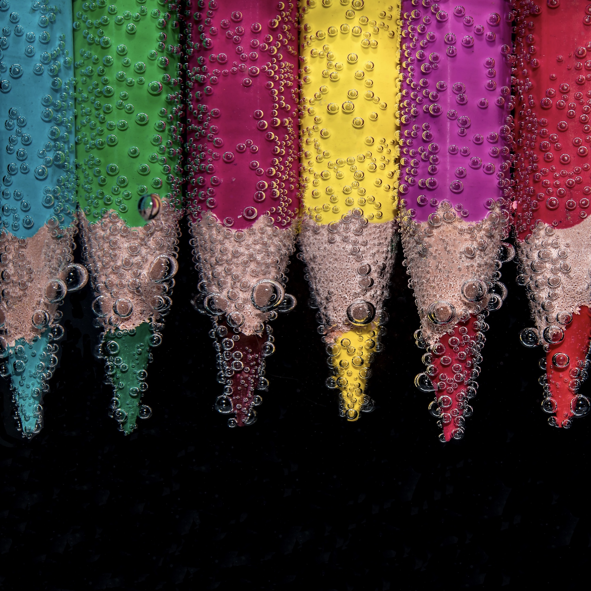 Foto: Reihe von Buntstiften, die unter Wasser liegen und von Luftbläschen umgeben sind
