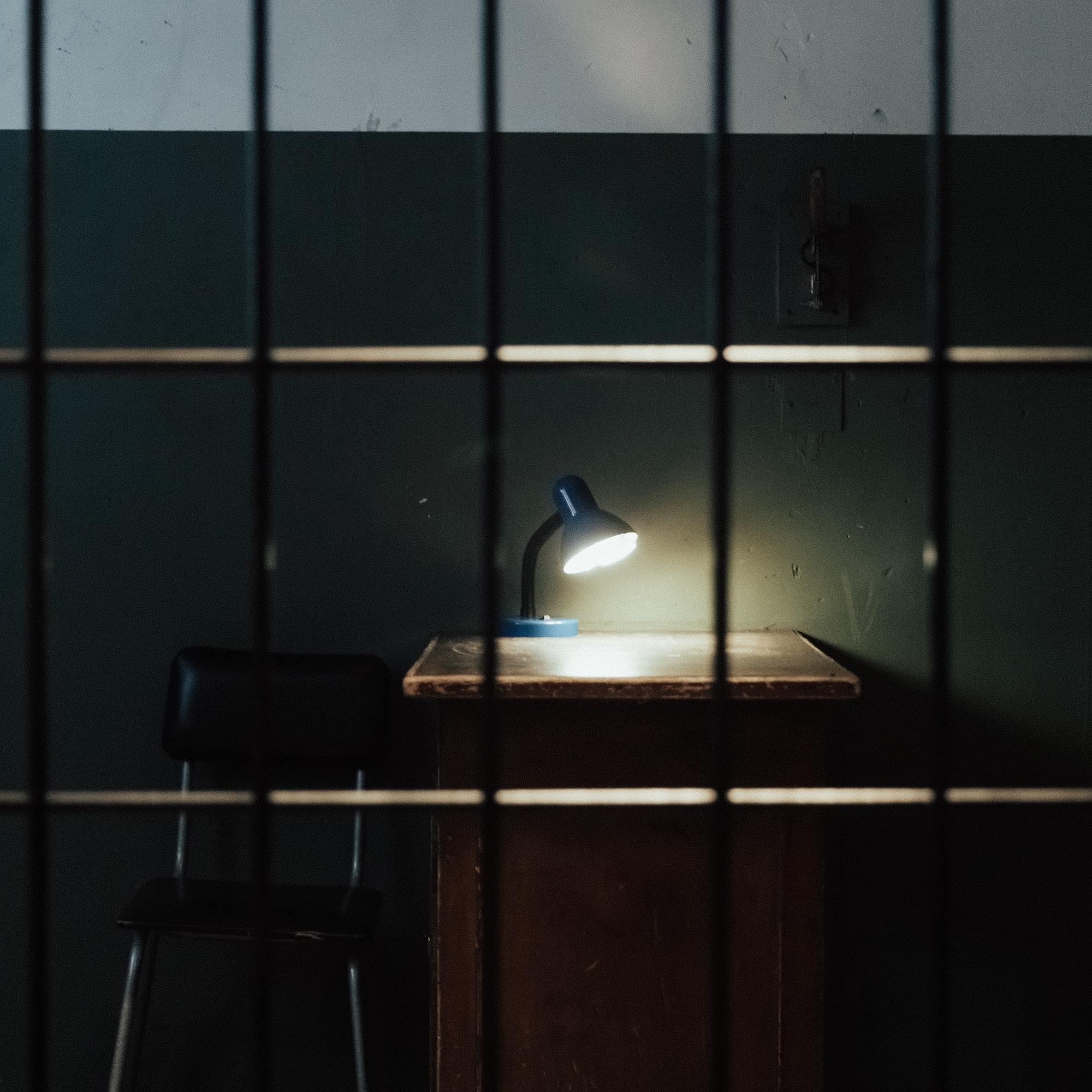 Foto: Schreibtisch mit leuchtender Lampe im Dunkeln hinter Gittern