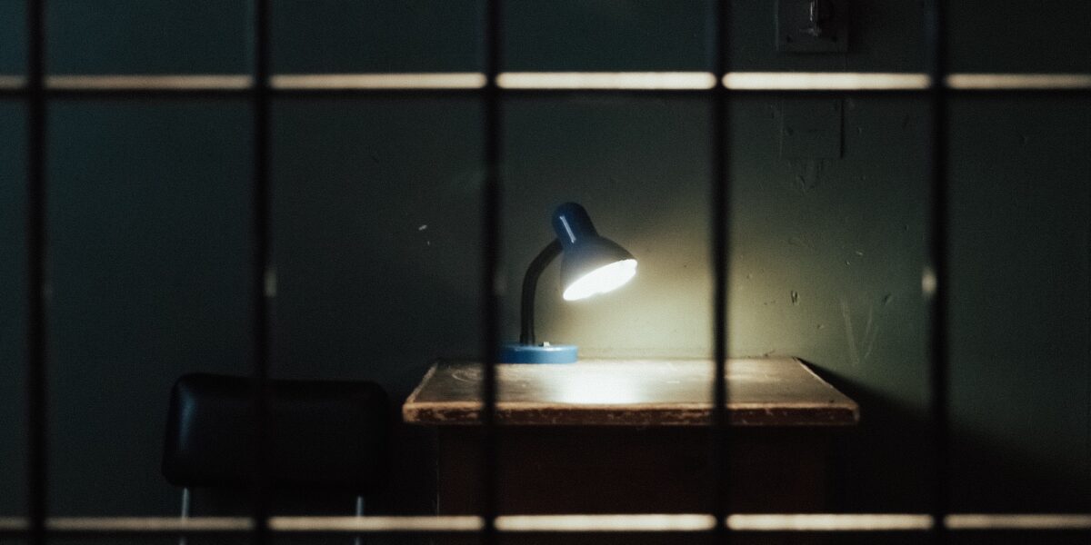 Foto: Schreibtisch mit leuchtender Lampe im Dunkeln hinter Gittern